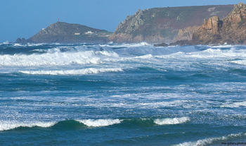 Cape cornwall waves This landscape photograph shows the powerful waves of Cape Cornwall crashing towards the rugged coast in the early afternoon during autumn. In the foreground, the sea appears restless with whitecaps and varying shades of blue, highlighting the dynamic nature of this part of the United Kingdom. The coastline features the cliffs near Sennen Cove, stretching out towards the distinctive headland of Cape Cornwall, which is visible in the background along with the well-known Cape Cornwall chimney landmark and the white building of the National Trust count house. This scene captures the natural beauty of Cornwall, with its dramatic cliffs and wild autumn sea, representing an iconic viewpoint of the region’s coastline.